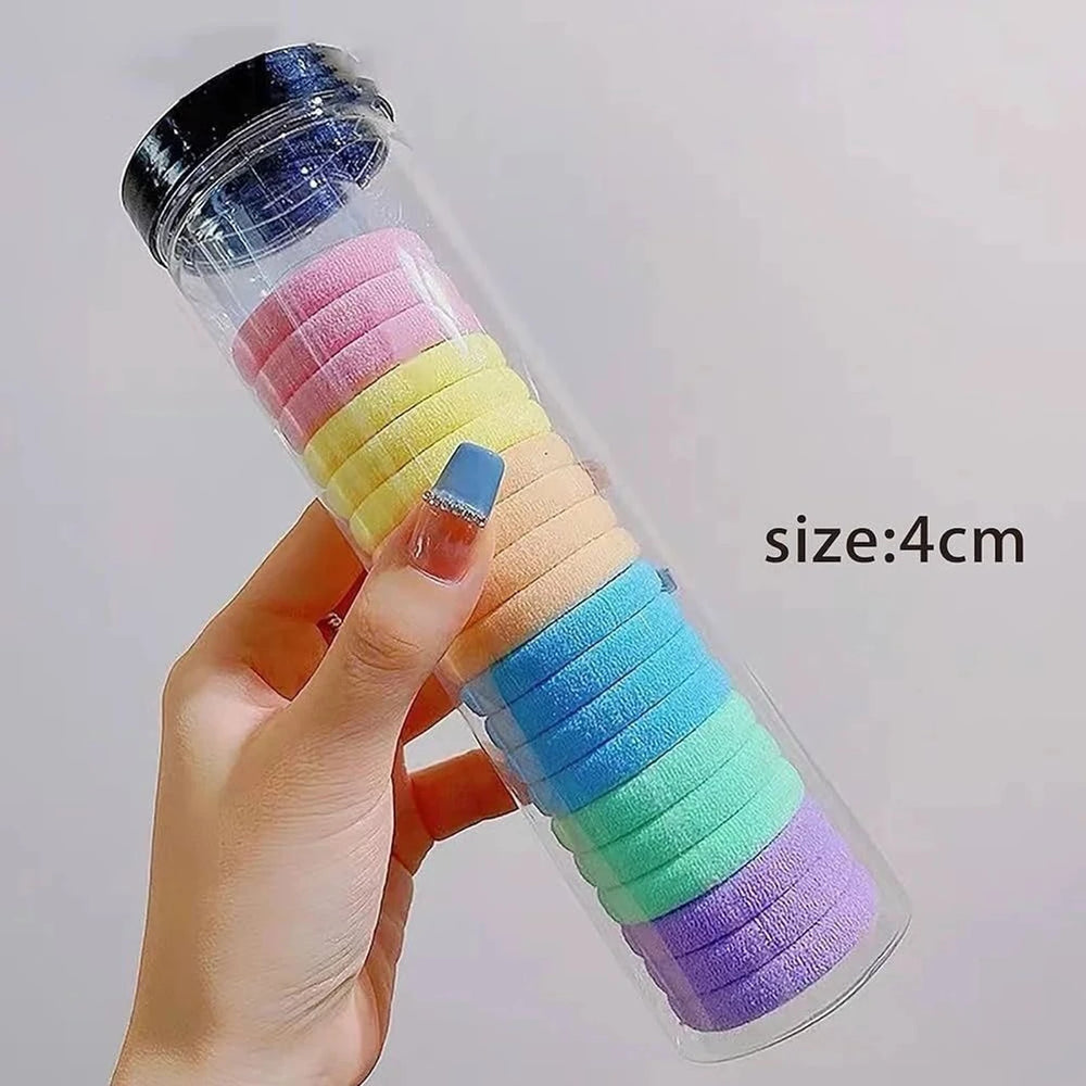 Clear cylindrical container with colorful hair ties held by a hand on a light gray background