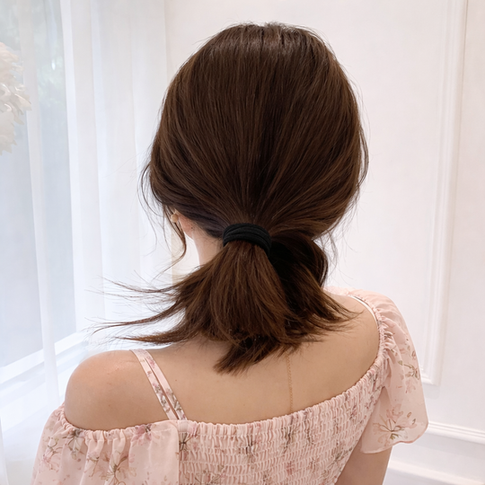 Woman with a ponytail wearing a light pink top against a white curtain background