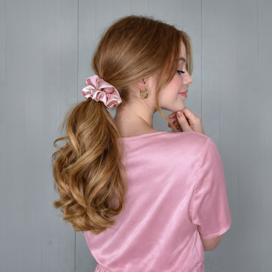 Woman with styled hair wearing a pink top against a gray background